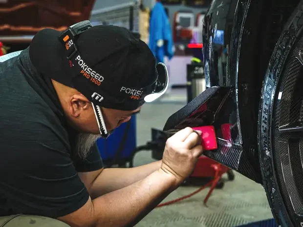 An Auto Obsessions technician laying paint protection film into a wheel arch by hand